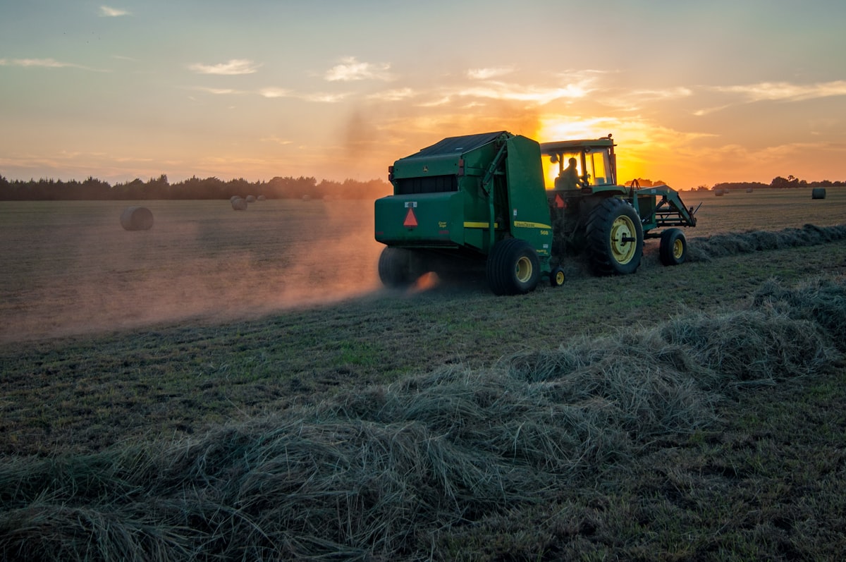 Traktor mit Strohballenpresse bei der Strohernte im Sonnenuntergang